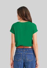 Groene top met korte mouwen, een ronde halslijn, een losse pasvorm en een licht cropped zoom, gecombineerd met blauwe jeans en een bruine riem.