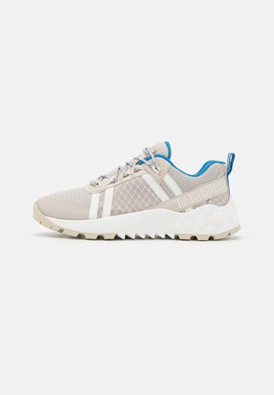 Jasnobeżowy sneaker Timberland z niebieską wyściółką, wzorzystą siateczkową cholewką, białą podeszwą i solidnym bieżnikiem, widok z boku na białym tle.