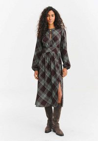 Sukienka z długim rękawem w kratę w kolorach bordowym i zielonym, z dekoltem typu keyhole, taliowaną talią oraz bocznym rozcięciem, zestawiona z brązowymi, sięgającymi kolan kozakami.