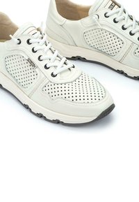 Zapatillas de cuero perforado blancas con cordones negros, suela de goma y detalles sutiles de logo. Incluyen un collar acolchado para mayor comodidad.