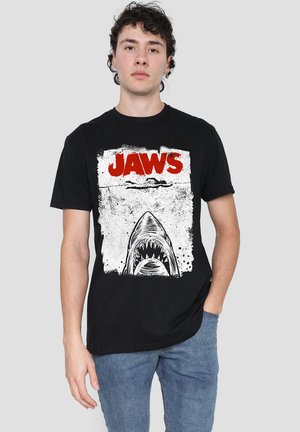 Black cotton t-shirt featuring a graphic of a shark with the text "JAWS" in red, set against a distressed white background. Simple cut design.