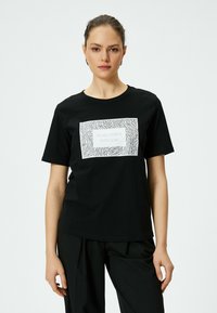 Sort bomulds t-shirt med et hvidt rektangulært grafisk motiv med zebra-striber og teksten "GØR ALLE TING MED KÆRLIGHED" i midten.