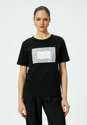 Sort bomulds t-shirt med et hvidt rektangulært grafisk motiv med zebra-striber og teksten "GØR ALLE TING MED KÆRLIGHED" i midten.