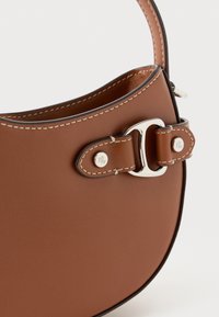 Bolsa de mão em pele castanha com costuras brancas, fivela prateada e detalhes na alça, sobre um fundo branco.