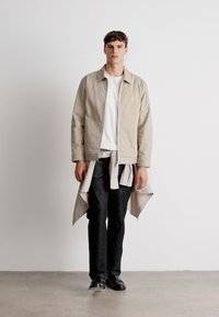 Jasno beżowa kurtka z zamkiem błyskawicznym noszona na białej koszulce, w zestawieniu z ciemnoniebieskimi dżinsami i czarnymi butami. Szara w paski koszula związana w pasie.