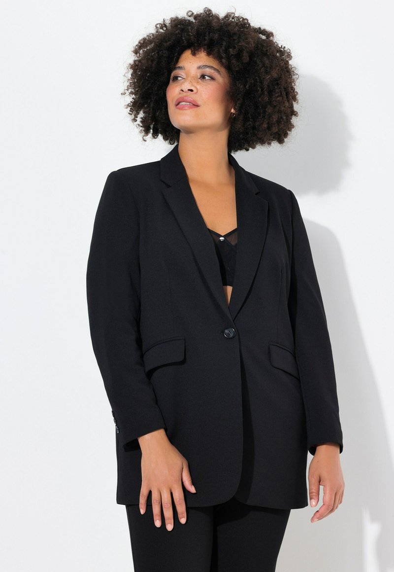Blazer nero con design sartoriale, rever a punta e due tasche frontali. Realizzato in tessuto liscio, presenta una chiusura a un bottone.