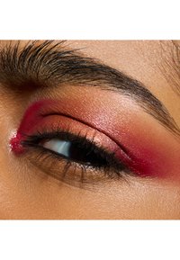 Gros plan sur un œil mettant en valeur des teintes chaudes et rouges de fard à paupières, des accents cuivrés métalliques et des cils bien définis sur un teint de peau lisse.