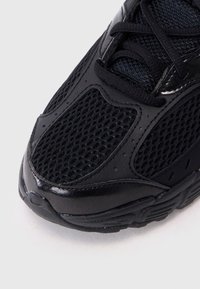 Basket noir de sport avec une tige en mesh et des accents brillants, des superpositions texturées et un bout arrondi. Système de laçage renforcé inclus.