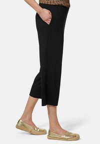 Zwarte capri-broeken met zijzakken, gemaakt van een gladde stof. Gecombineerd met glanzende gouden espadrilles.