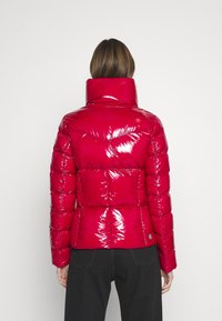 Röd puffjacka med glänsande ytfinish, hög krage och quiltat mönster. Har horisontella och diagonala sömmar.