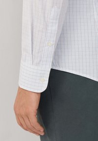 Wit geruit overhemd met blauwe en rode ruitpatronen. Bevat knoopmanchetten en een gladde textuur, gecombineerd met een donkergrijze stof hieronder.