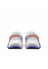 Vista trasera de zapatillas deportivas de malla blanca con acentos en naranja y azul. Presenta una suela texturizada con un patrón de zigzag. Forma redondeada y cuello acolchado.