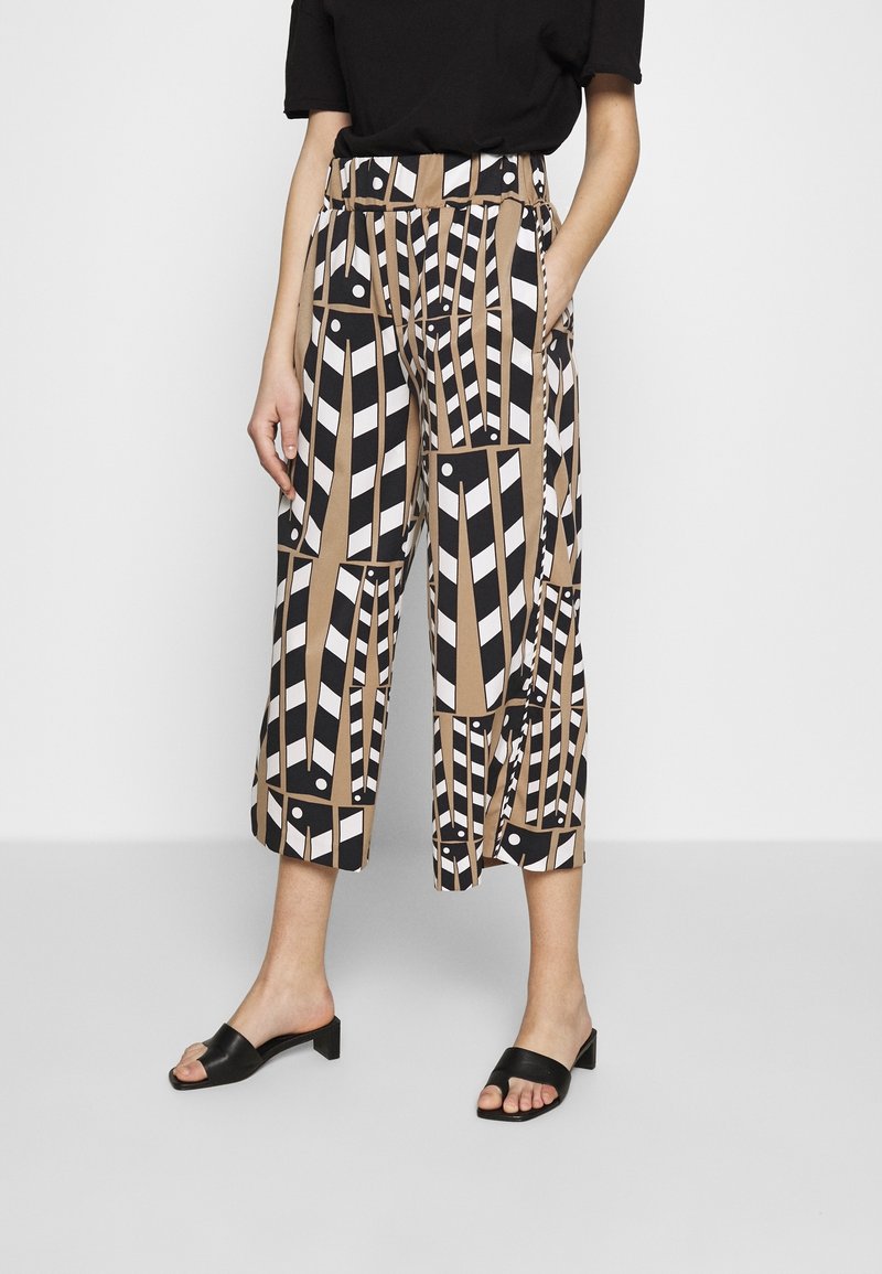 Cropped trousers with a geometric pattern in beige, black, and white; features side pockets, high waist, and a relaxed fit.