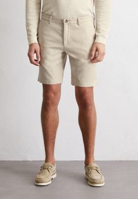 Shorts en coton khaki avec une coupe droite, fermeture �à bouton sur le devant, deux poches latérales et une texture lisse. Portés avec des chaussures en daim beige.