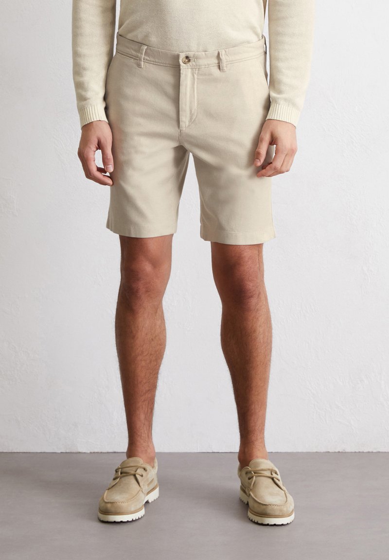 Khaki katoenen shorts met een rechte snit, voor knoopsluiting, twee zijzakken en een soepele textuur. Gecombineerd met beige suède schoenen.