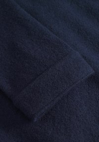 Sötétkék gyapjú szövet, puha, texturált felülettel. Hajtott széle és látható szálai vannak, így meleg és otthonos megjelenést kölcsönöz.