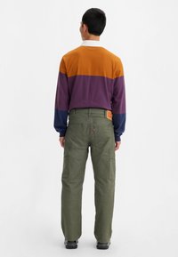 Långärmad färgblockerad skjorta med orange, lila och blå sektioner, i kombination med gröna cargobyxor med flera fickor och en brun etikett.