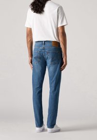 Blå denim jeans med rak passform, med bakfickor och en läderpatch vid midjan. Matchat med en enkel vit t-shirt.