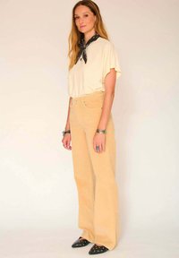 T-shirt beige surdimensionné associé à un jean flare taille haute de couleur beige clair. Chaussures à talons noires avec des clous en argent et une écharpe noire autour du cou.