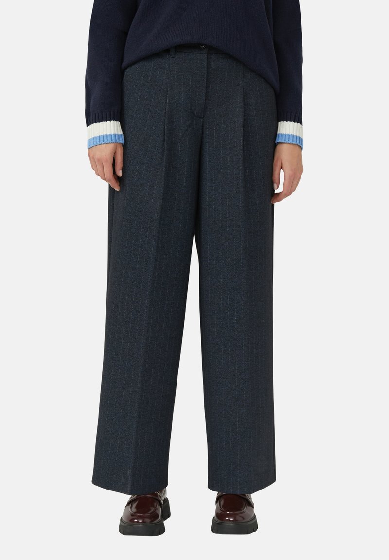 Wijde donkerblauwe pantalon met krijtstrepen en een nauwkeurige snit. Draagt onder een marineblauwe trui en glanzende bordeauxrode schoenen. Glad textuur en gestructureerd ontwerp.