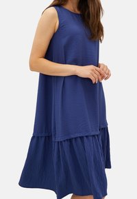 Hihaton sininen mekko, jossa on teksturoitu pinta, kerroksittain leikattu helma ja löysä istuvuus, kevyt materiaali, ihanteellinen lämpimiin säihin.