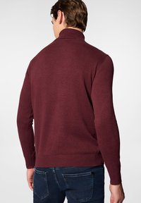 Bordowy sweter dzianinowy z wysokim kołnierzem i ściągaczami, w połączeniu z ciemnoniebieskimi dżinsami, eksponujący gładką teksturę i dopasowany krój.