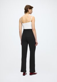 Schwarze, hoch taillierte Hose aus einem weichen, strukturierten Stoff mit leicht ausgestelltem Saum. Kombiniert mit einem weißen, eng anliegenden Tanktop.