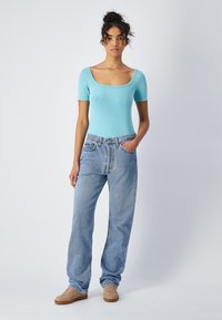 Jasnoniebieski bodysuit z krótkim rękawem i kwadratowym dekoltem, zestawiony z jasnoniebieskimi dżinsami z wysokim stanem i beżowymi sneakersami.