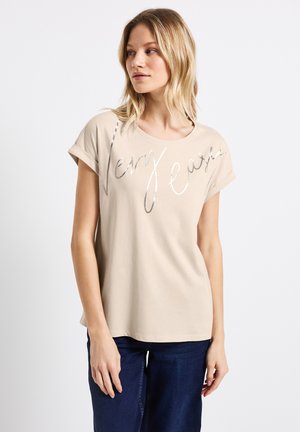 Camiseta de manga corta beige hecha de un tejido suave, con un estampado metálico en plata que dice "Muy Fácil" en la parte delantera. Diseño simple.