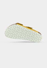 Κίτρινο σανδάλι με διπλές λουρίδες που απεικονίζεται από το πλάι, τονίζοντας το λεπτομερές λευκό υφασμάτινο μοτίβο της σόλας σε λευκό φόντο.