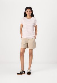 Stripet lys rosa t-skjorte, beige shorts og svarte joggesko med brune såler. Enkel design, avslappet passform og uformell stil.