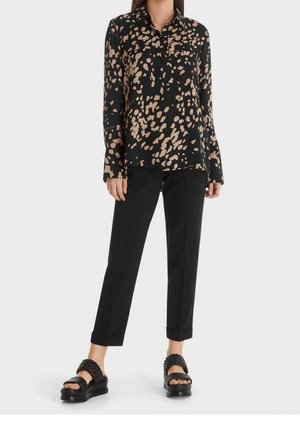 Kobieta ubrana w czarne spodnie, czarno-beżową bluzkę z długim rękawem w abstrakcyjny wzór oraz czarne sandały na platformie z plecionymi paskami.