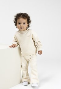 Lichtbeige sweatshirt en bijpassende broek van zacht materiaal. Beschikt over een ronde halslijn en geribbelde manchetten, met witte sneakers.