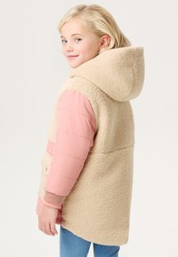 Manteau en polaire beige avec des manches et une capuche en tissu matelassé rose, présentant une finition texturée et des poches avant. Tissu lisse sur les manches.