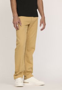 Pantalon en coton beige avec une coupe droite, porté avec des baskets blanches. Le tissu a une texture lisse et de subtils détails de couture.