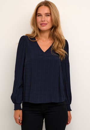 Navyblauwe blouse met V-hals, textuurstof en lange mouwen met elastische manchetten. Effen kleur met een subtiel ruitpatroon.