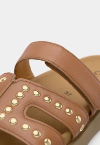 Καφέ δερμάτινο σανδάλι με δύο λουριά, διακοσμημένο με χρυσούς τρουκς στο πάνω μέρος. Διαθέτει επενδυμένο πάτο, μέγεθος 37 σημειωμένο στο εσωτερικό.