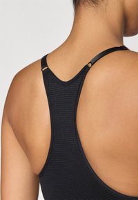 Svart racerback sportsbh med teksturert stoff, justerbare stropper med metalliske detaljer og en jevn, konturert ryggdesign.