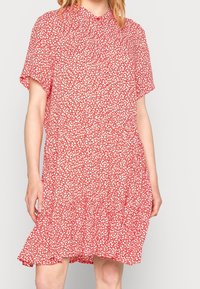 Robe florale rouge avec des manches courtes, un col rond et un ourlet à volants froncés. Présente de petits motifs floraux blancs sur l'ensemble.