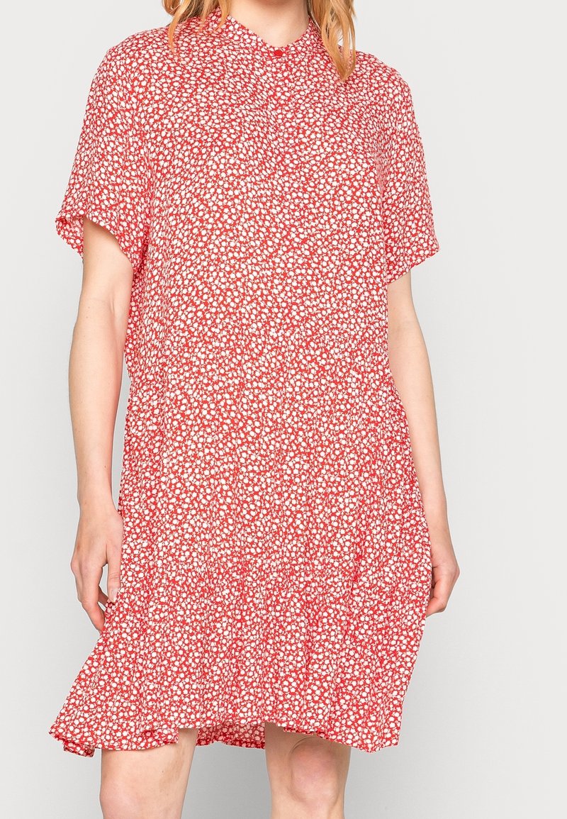 Robe florale rouge avec des manches courtes, un col rond et un ourlet à volants froncés. Présente de petits motifs floraux blancs sur l'ensemble.