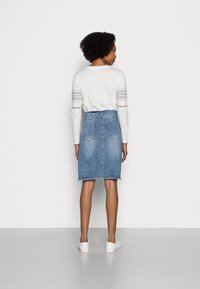 White long-sleeve top with patterned sleeves paired with a light blue denim skirt, featuring a frayed hem and back pockets. White sneakers.