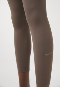 Bruna leggings i elastiskt material med smal passform, längd till mitten av vadderna och en liten grå Nike-logotyp på sidan.