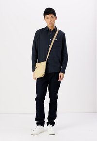 Camicia blu navy a bottoni, borsa a tracolla color khaki, jeans scuri e sneakers bianche. Design semplice con colori neutri e vestibilità casual.