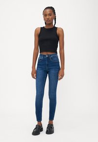 Melna bez piedurknēm crop-top krekls, augsto vidukļu zili šaurie džinsi un melni loaferi. Gluda tekstūra un piegulošs dizains.