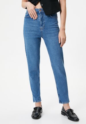 Jean bleu taille haute avec une coupe droite, en tissu denim. Doté d'une fermeture à bouton et d'un léger délavage. Associé à des mocassins noirs brillants.