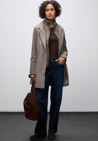 Cappotto grigio chiaro con colletto a punte, sovrapposto a una giacca imbottita marrone, abbinato a jeans blu scuro e a una borsa in suede marrone.