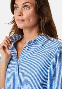 Camicia a righe blu e bianche con colletto classico, tessuto morbido e dettagli sul patte. Tessuto testurizzato con linee verticali.