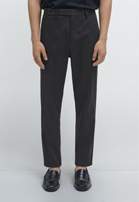 Zwarte slim-fit broek met een platte voorkant, voorzien van zijzakken en een enkele knoopsluiting. Gekocht met zwarte instappers. Glad textuur.
