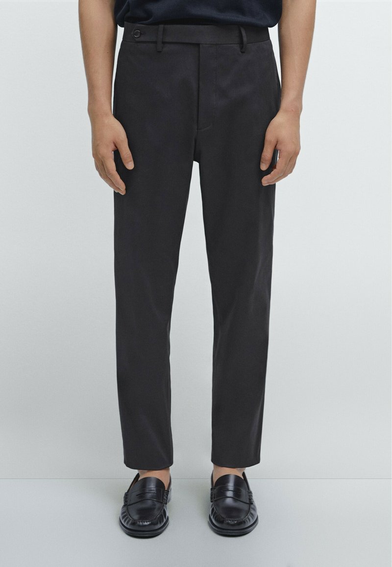 Zwarte slim-fit broek met een platte voorkant, voorzien van zijzakken en een enkele knoopsluiting. Gekocht met zwarte instappers. Glad textuur.
