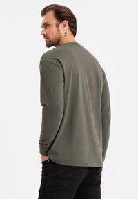 T-shirt a maniche lunghe in cotone verde oliva con vestibilità rilassata, scollo rotondo e cuciture piatte. Indossato con jeans neri, mostrando un colore solido.